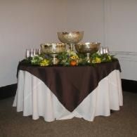Decorated round table with gold bowls, candles, and greenery on brown and white tablecloths