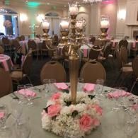 Banquet hall table centerpiece with pink and white flowers beneath a brass candelabra
