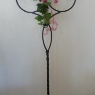 Decorative black metal stand with pink flowers and green leaves against a plain white wall