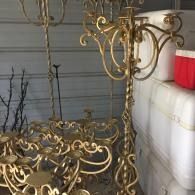 Ornate gold metal furniture on a porch beside a white wall and red cooler