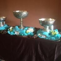 Silver trophy cups on a table with turquoise fabric decorations against a brown background
