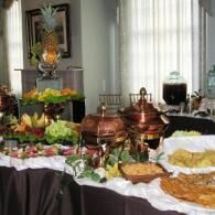 Buffet table with copper chafing dishes, fruit centerpiece, and assorted food trays at a formal event