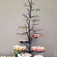 Black tree-shaped dessert stand holding assorted cupcakes in a neutral indoor setting