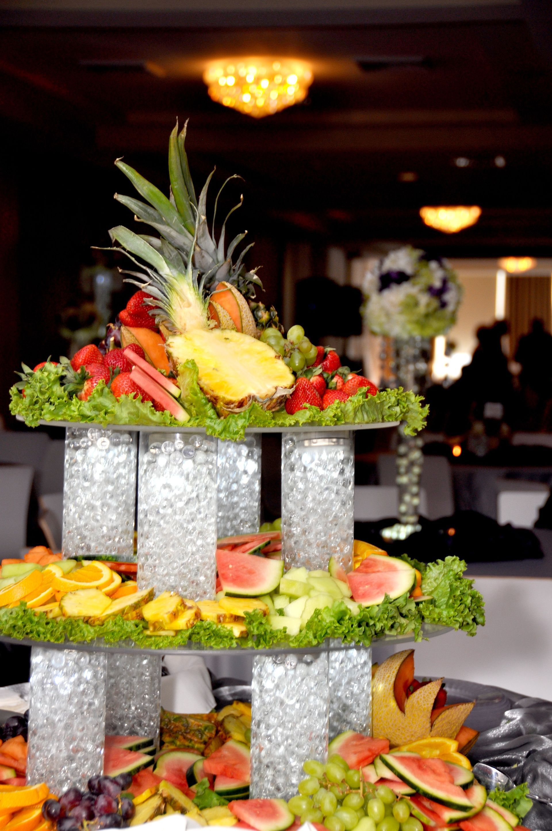 Tiered fruit display with pineapple, citrus, and red fruit on a table at an indoor event