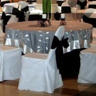 Round banquet table with silver tablecloth and black-and-white chair covers in a reception hall
