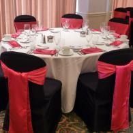 Round banquet table set with white cloth and red-black chair covers in a decorated event room