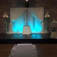 Decorated stage with white drapes, blue uplighting, and a small table at center