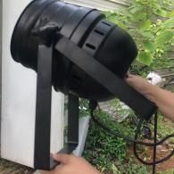 Person adjusting a black wall-mounted device outdoors near greenery