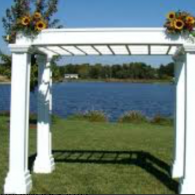 White garden arbor with sunflowers, overlooking a blue lake and grassy shore