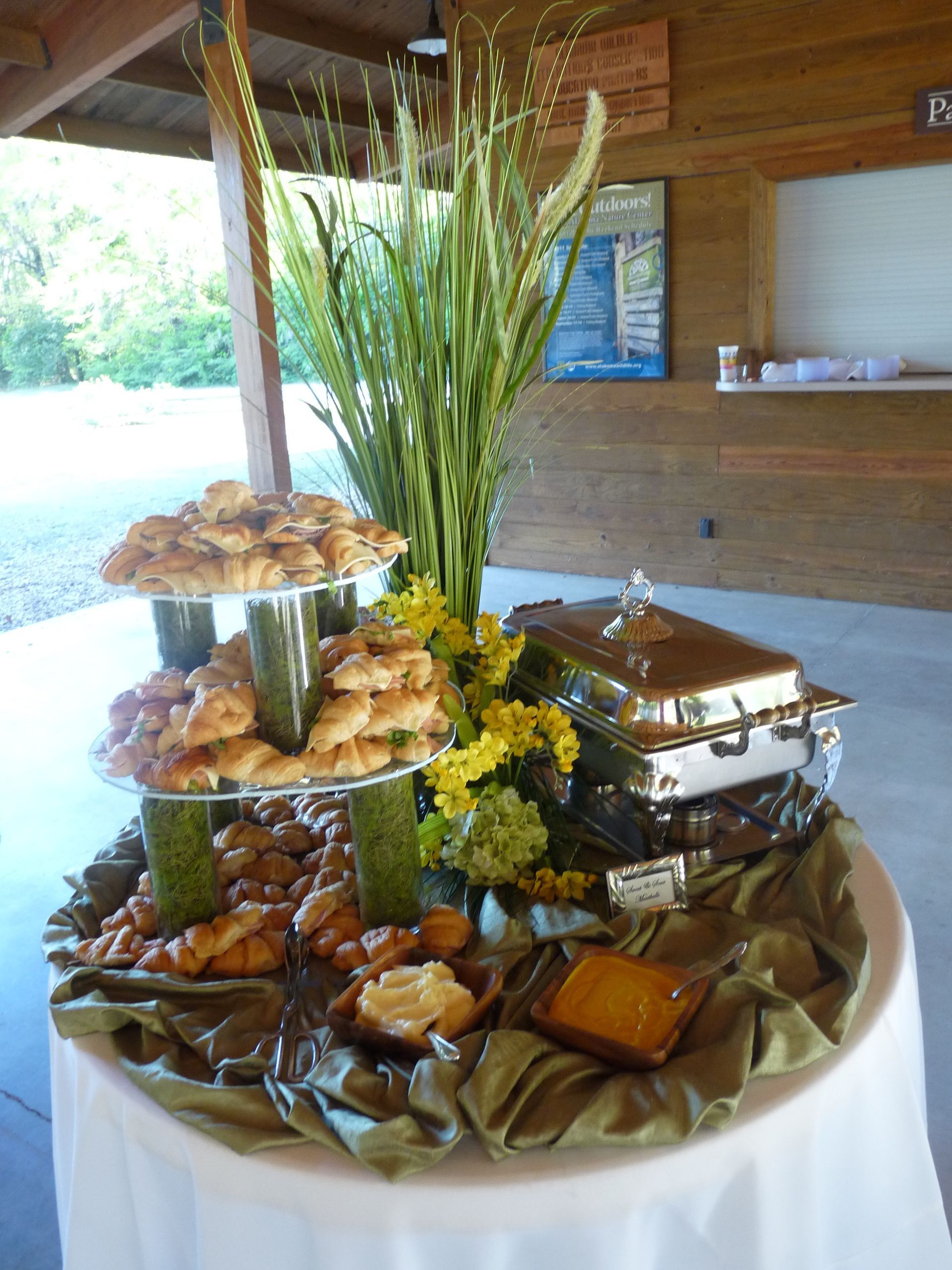 Tiered buffet display with fried appetizers, sandwiches, and a tall green centerpiece under a pavilion