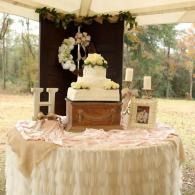 Decorated wedding cake on a draped table beneath a floral arch at an outdoor reception
