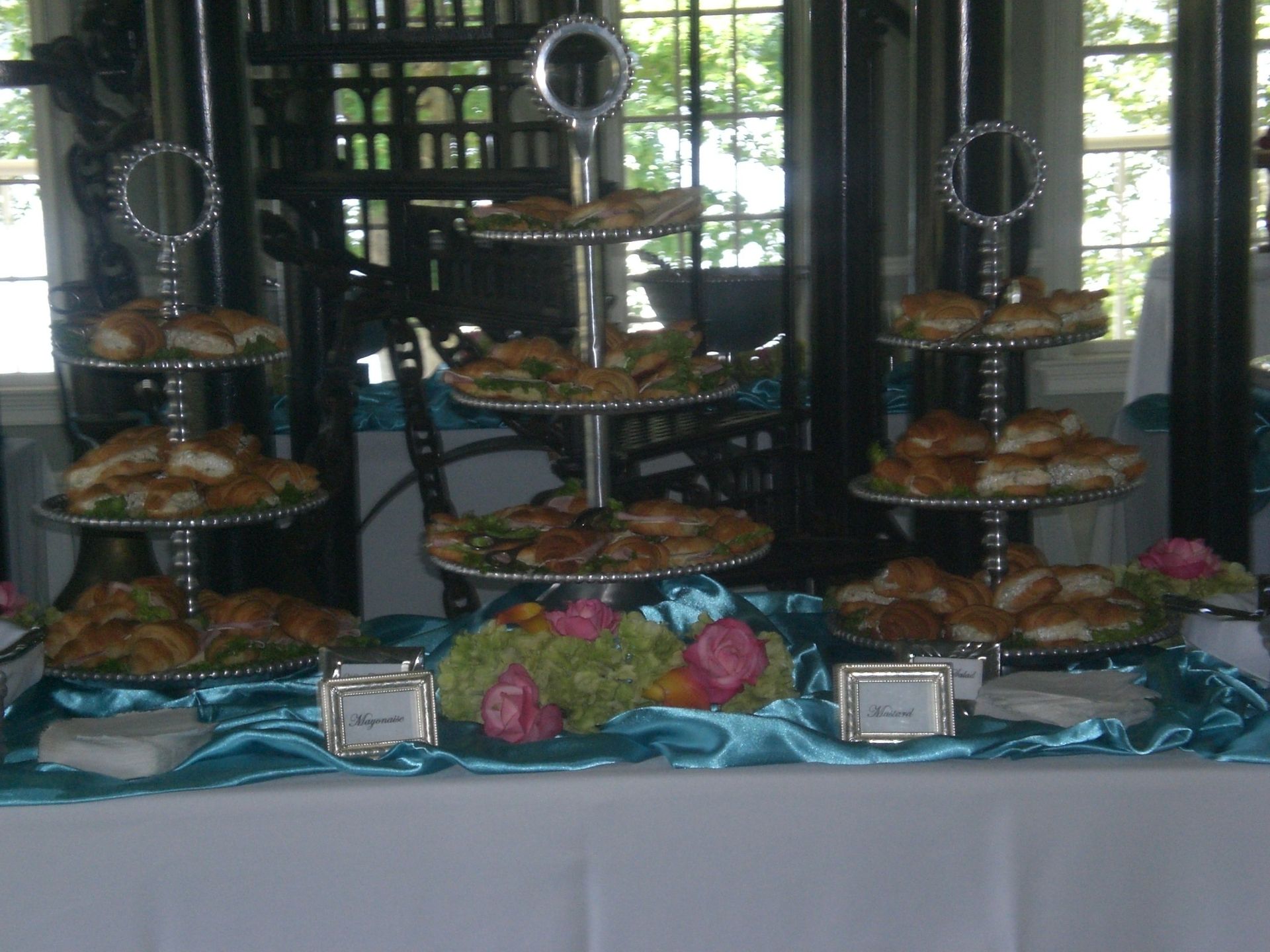 Tiered dessert buffet with trays of pastries and tarts on a table decorated with blue cloth and flowers