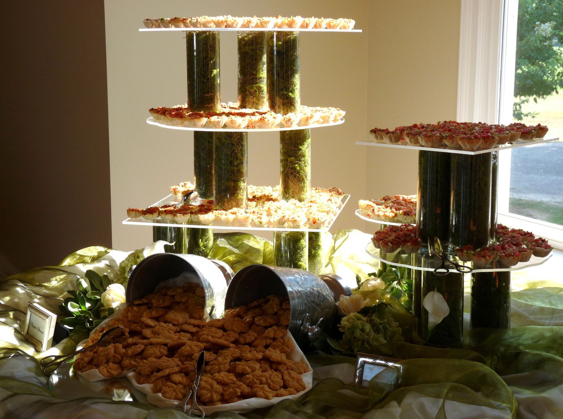Tiered food display with stacked green rolls and plates of appetizers on a sunlit table