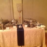 Buffet table with covered chafing dishes and a tall crystal lamp centerpiece