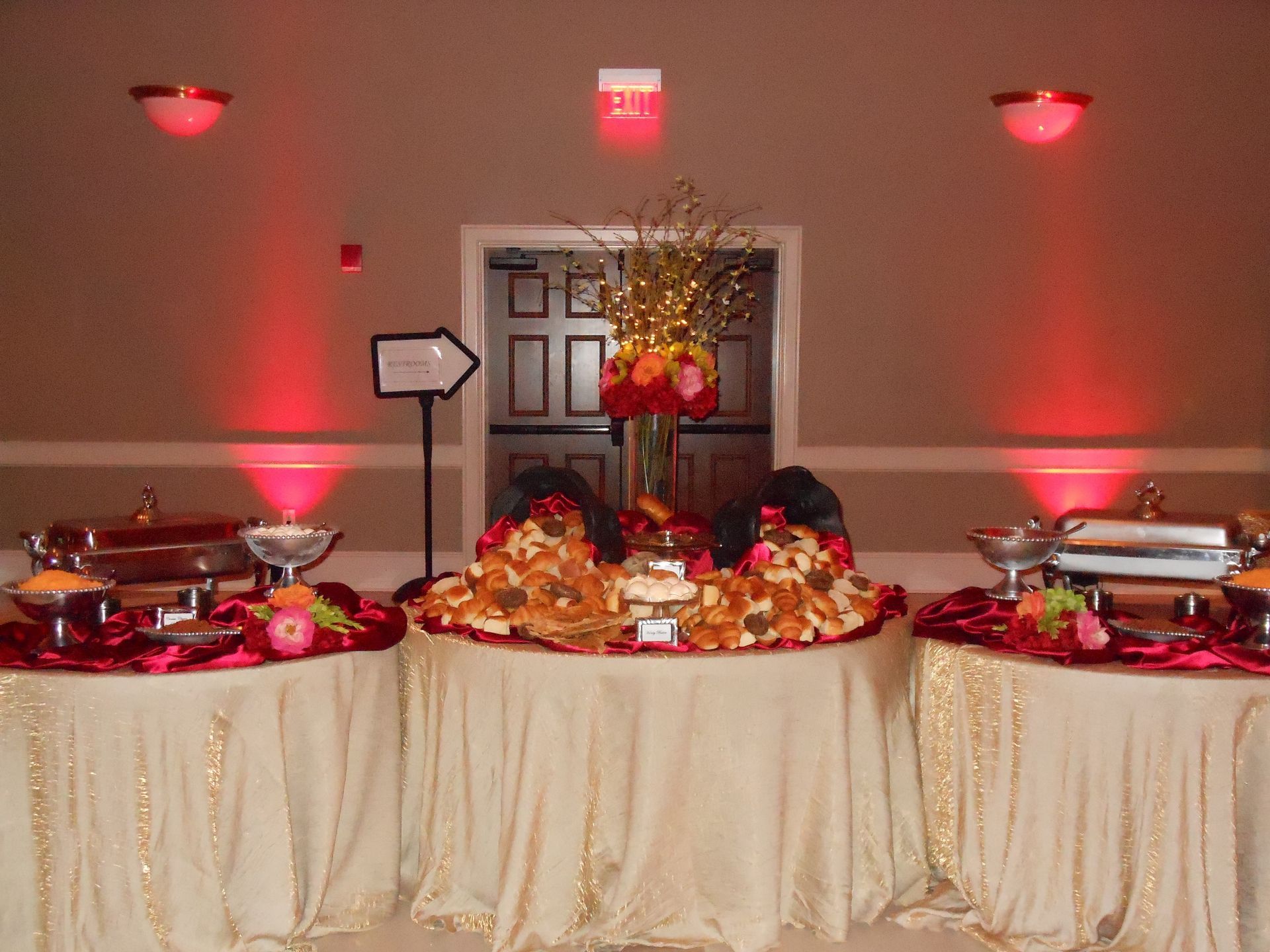 Buffet table with floral centerpiece, red accents, and covered serving dishes in a banquet hall