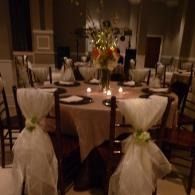 Elegant dining room with a round table set for a formal event, white chair covers, and a floral centerpiece