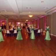 Elegant banquet hall with green cocktail tables, purple uplighting, and guests mingling on a polished wood floor