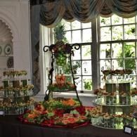 Elegant dessert display with flowers and tiered trays by a bright window in a draped room