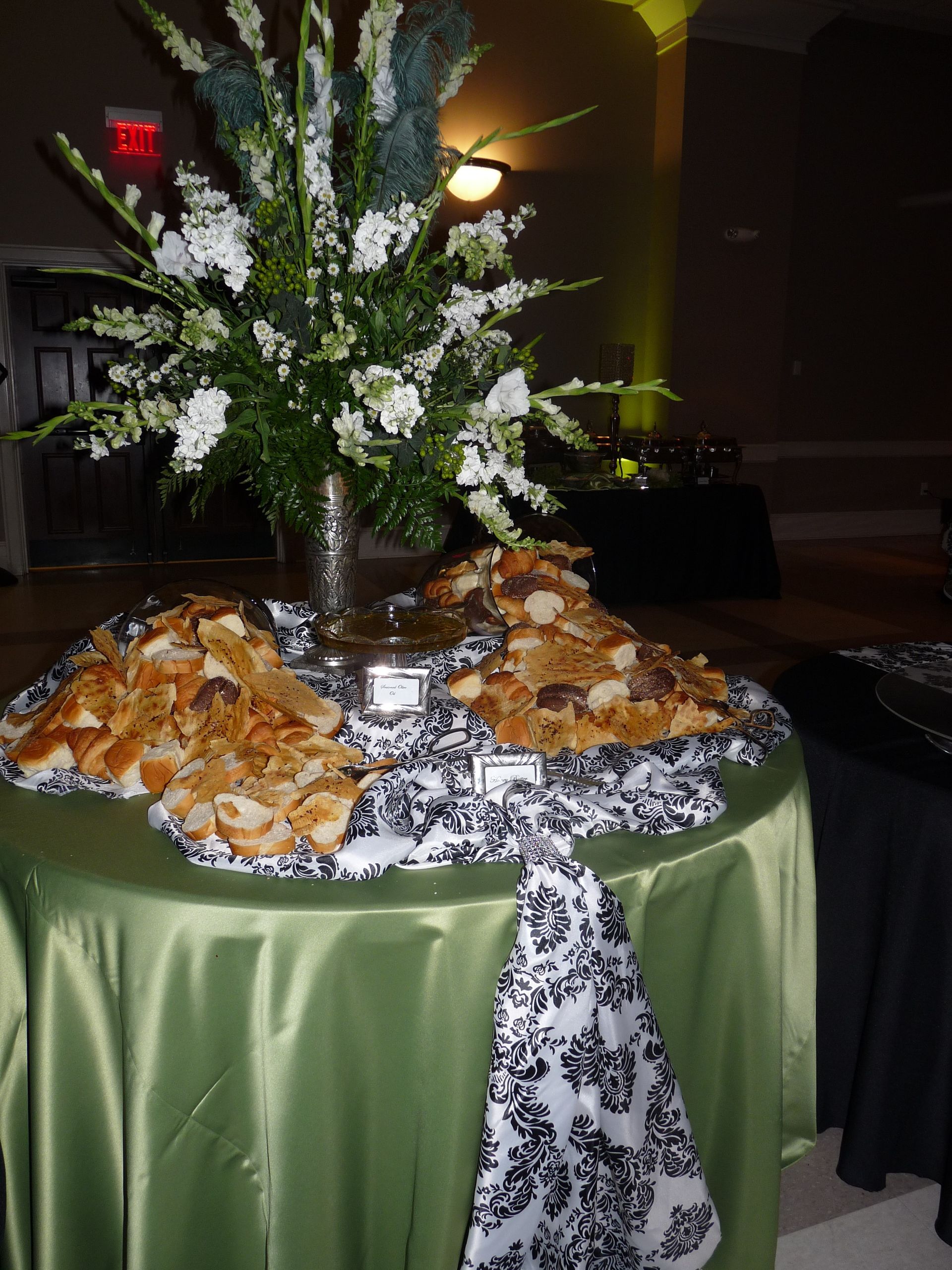 Buffet table with green cloth, floral centerpiece, and trays of appetizers at an indoor event