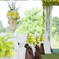 White chair with green floral bouquet and brown ribbon in a decorated outdoor setting