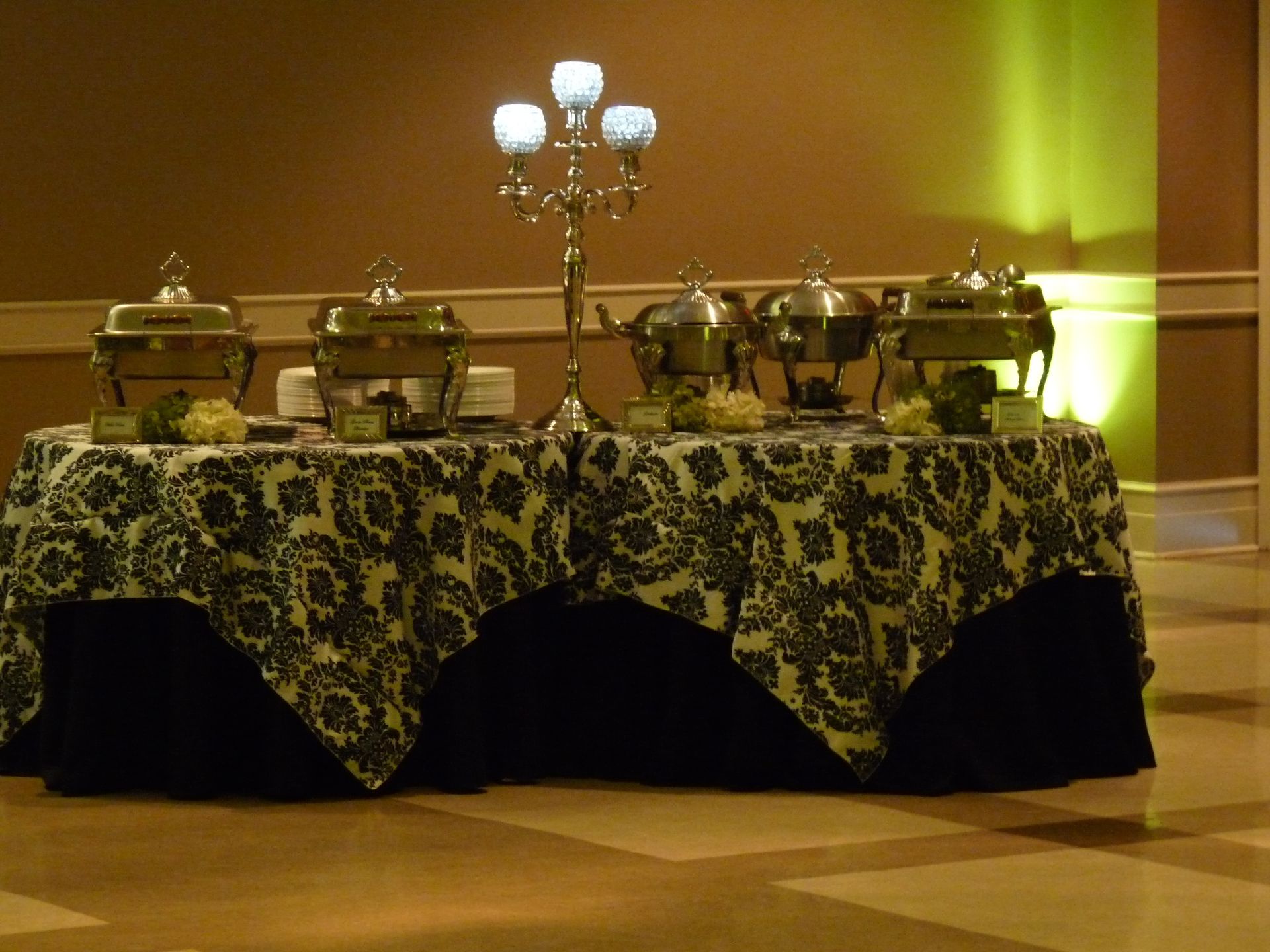 Buffet table with covered serving dishes and candelabra, draped in patterned cloth in a warm-lit room