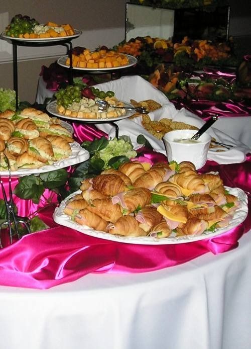Buffet table with assorted pastries, fruit, and appetizers on white platters and pink tablecloths