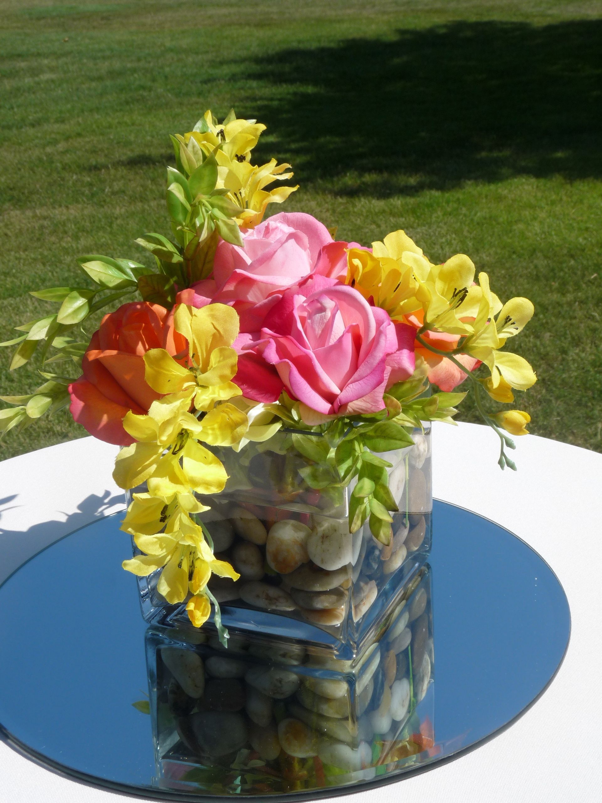 Colorful flower arrangement in a glass vase on a reflective table outdoors