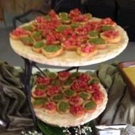 Two tiered platters of bite-sized appetizers topped with red and green garnish.