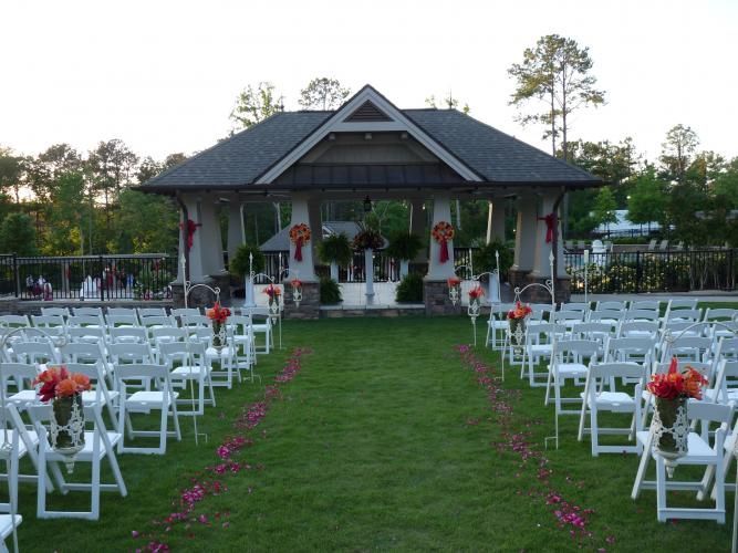 Outdoor wedding aisle with white chairs lined on both sides leading to a decorated pavilion at dusk
