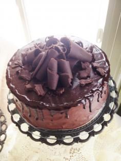 Chocolate cake topped with chocolate curls and drips on a decorative platter