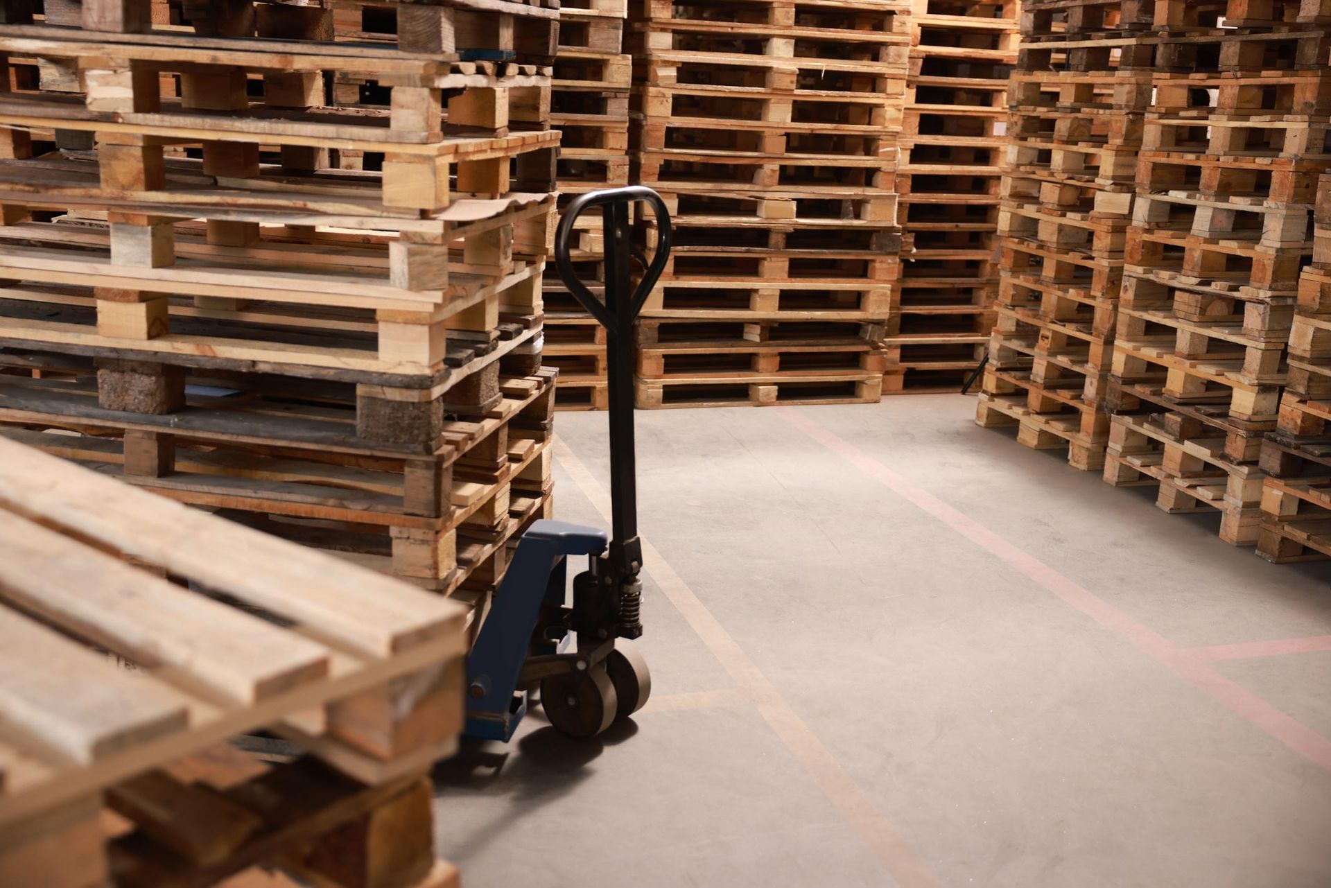A warehouse filled with lots of wooden pallets and a hand truck.