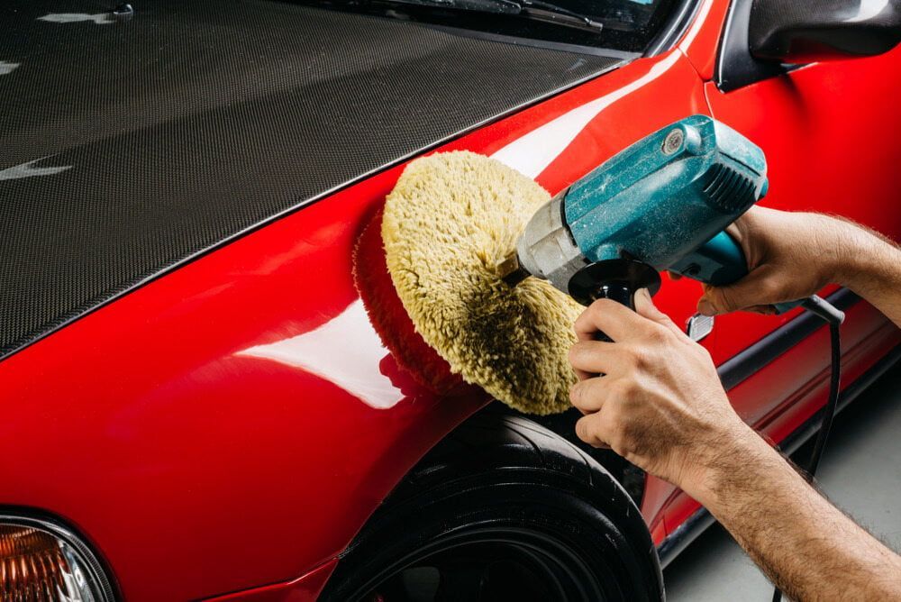 A Person Is Polishing A Red Car With A Sponge — K & D Auto Repair in Cardiff, NSW