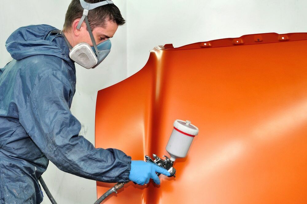A Man Wearing A Mask Is Spray Painting A Car Hood — K & D Auto Repair in Cardiff, NSW