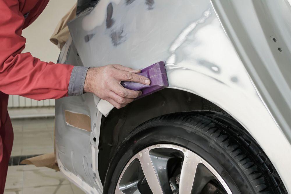 A Man Is Polishing The Fender Of A Car With A Sponge — K & D Auto Repair in Cardiff, NSW