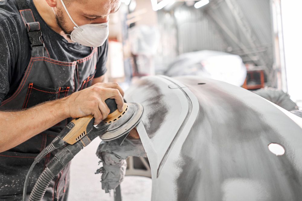 A Man Wearing A Mask Is Sanding A Car With A Sander — K & D Auto Repair in Cardiff, NSW