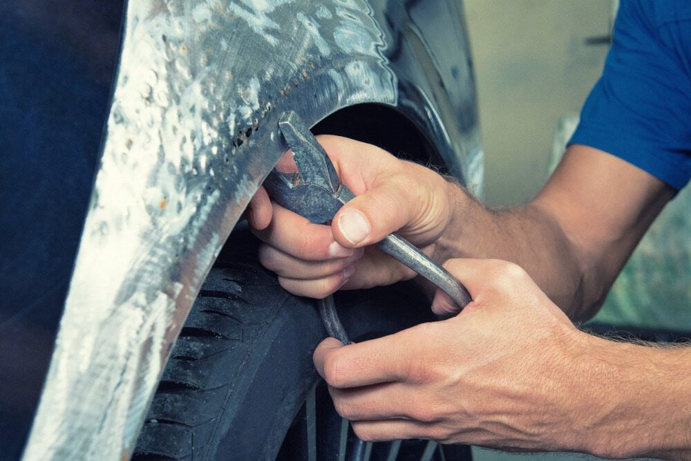 A Man Is Working On A Car Fender With A Wrench — K & D Auto Repair in Cardiff, NSW