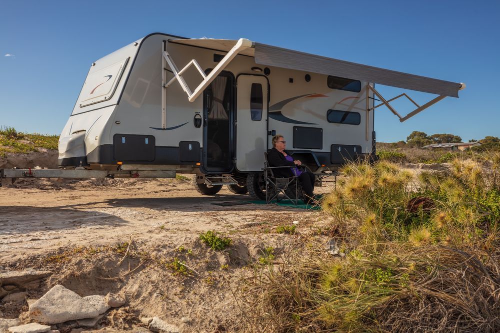 Person in Wheelchair Outside Camper Van, Awning Extended, Parked on Dirt. Bright Sunny Day — Darren's Caravan Repairs in Warners Bay, NSW
