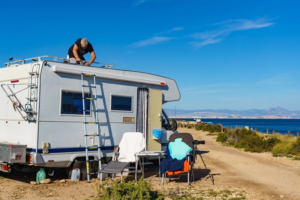 Man on Caravan Roof Near Coast, Repairing Something — Darren's Caravan Repairs in Warners Bay, NSW