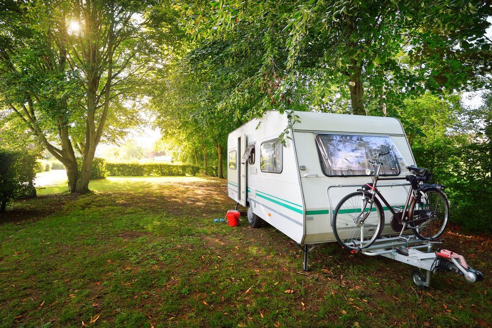 Camper Trailer With Bicycles Parked on a Grassy Campsite, Surrounded by Trees — Darren's Caravan Repairs in Warners Bay, NSW