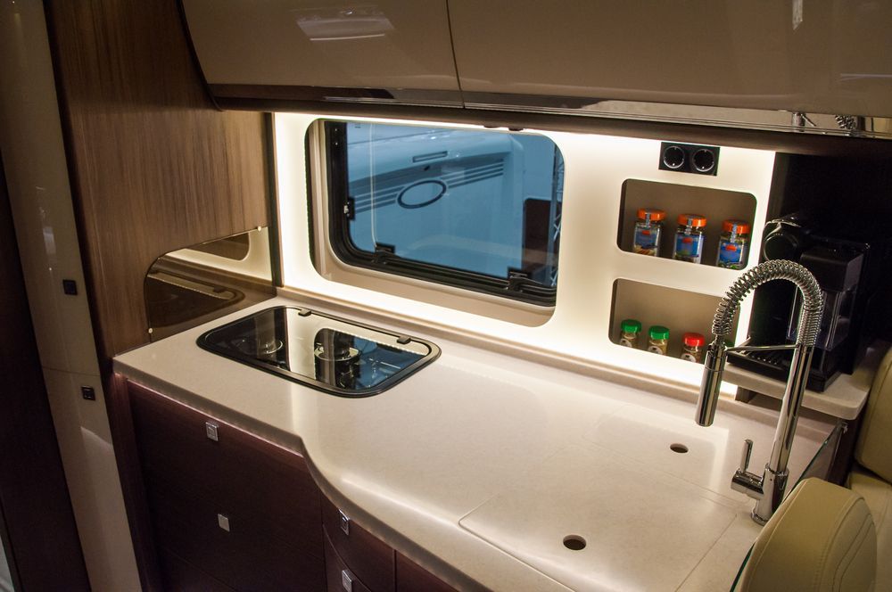 RV Kitchen Interior with White Countertop, Stainless Steel Faucet, Window, Spice Racks, and Stovetop — Darren's Caravan Repairs in Warners Bay, NSW