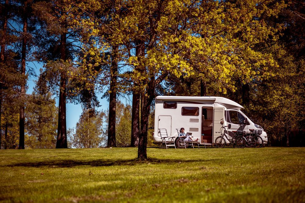 RV Parked on Grassy Area Under Trees; Bikes, Chairs, and a Person Are Visible — Darren's Caravan Repairs in Warners Bay, NSW