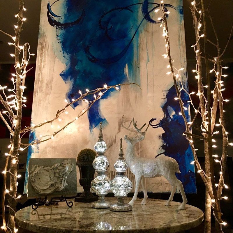 Round table with a winter-themed display, illuminated by string lights, against an abstract blue and white painting.