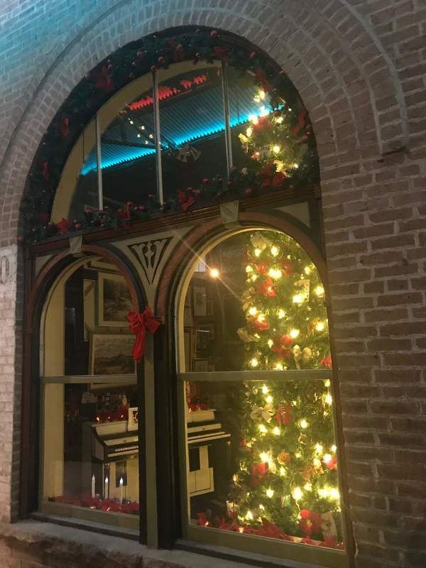 Christmas tree and decorations in a large arched window of a brick building.