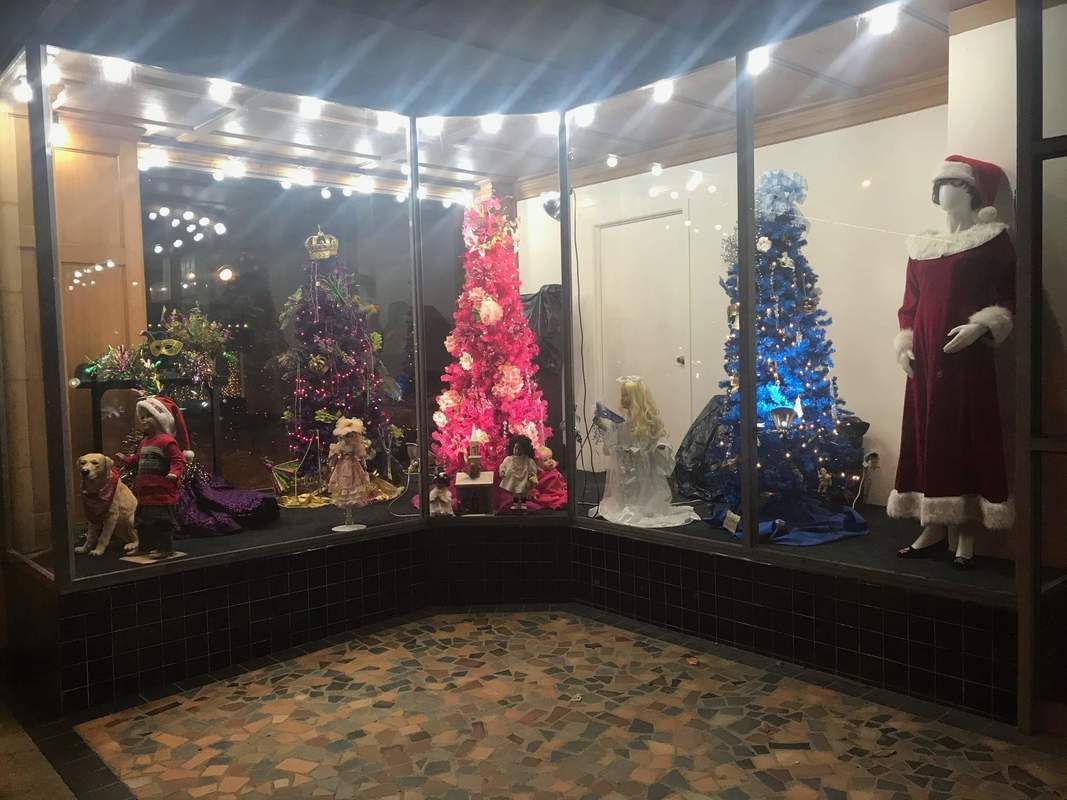 Christmas window display with decorated trees, mannequins in festive attire, and lights.