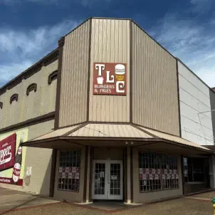 TLC Burgers & Fries restaurant exterior. Tan and white building with a sign and awning. Double doors.
