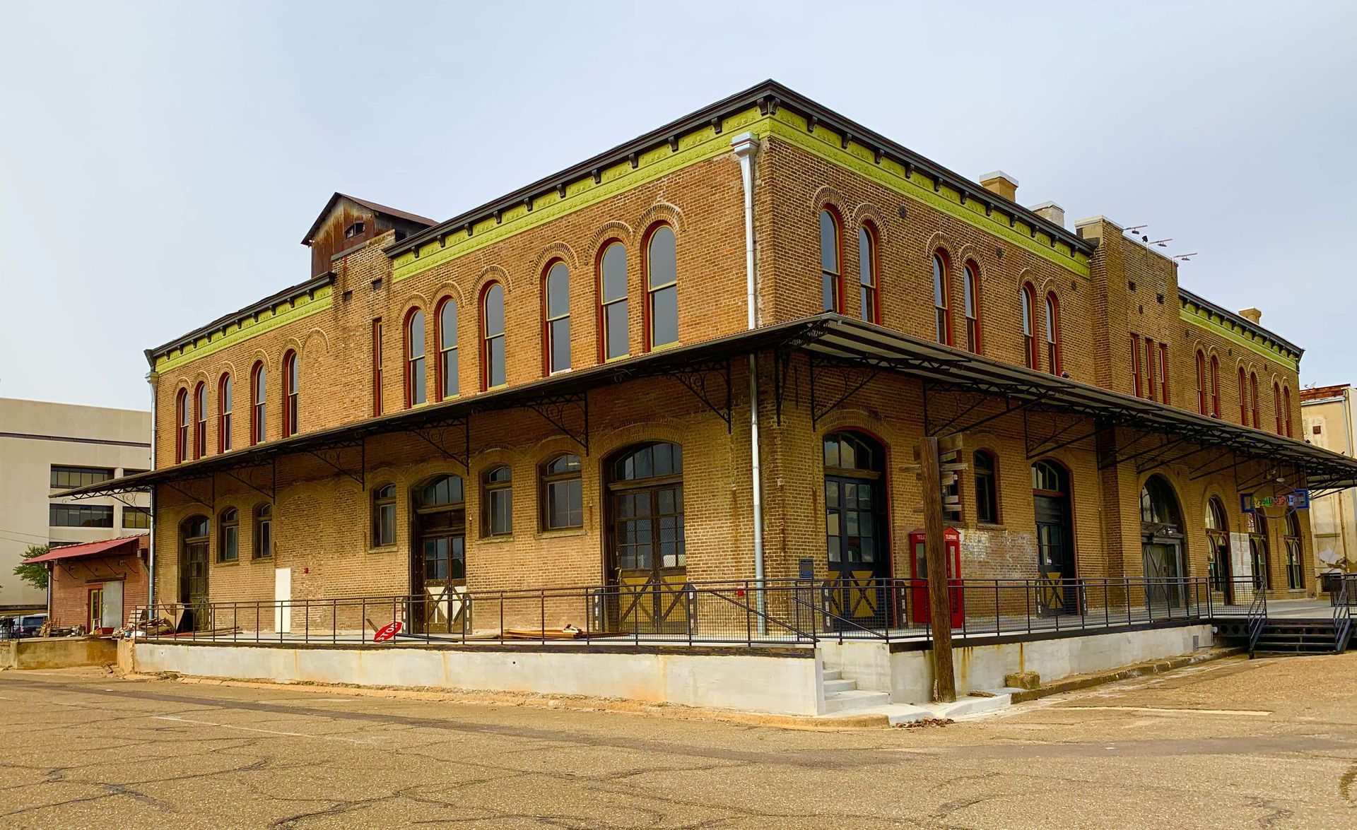 Brick building with arched windows and a wraparound porch, under a cloudy sky.