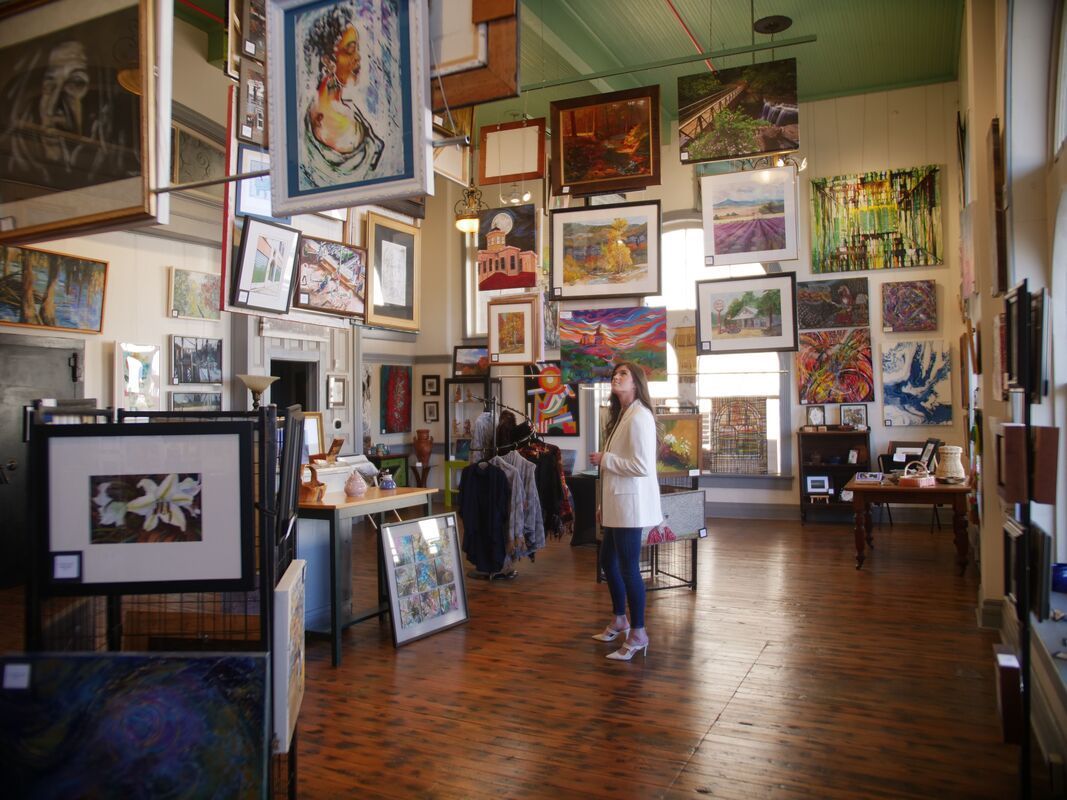 An art gallery with paintings hanging from the ceiling and walls. A person stands in the center.