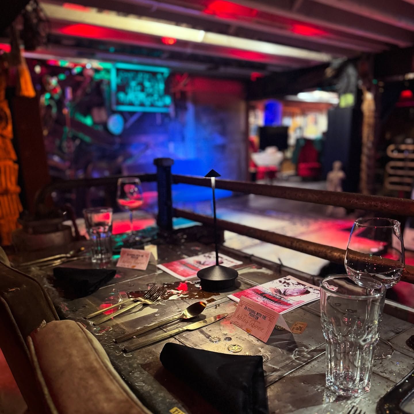 A dimly lit room with a table set for dinner. Red and blue lights illuminate the background.