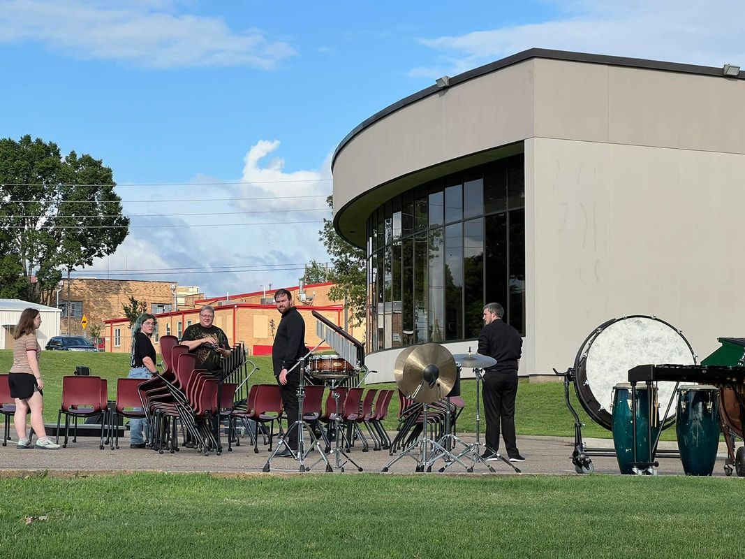 A band with instruments on a grassy area near a modern building with large windows.