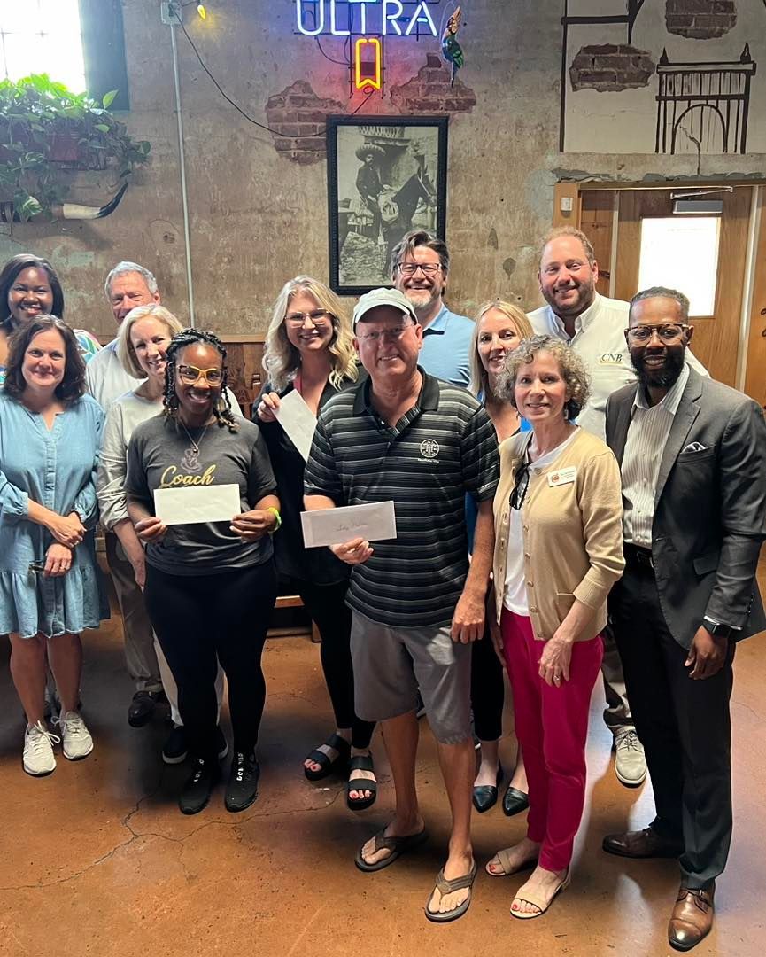 Group of people holding checks indoors, smiling. 